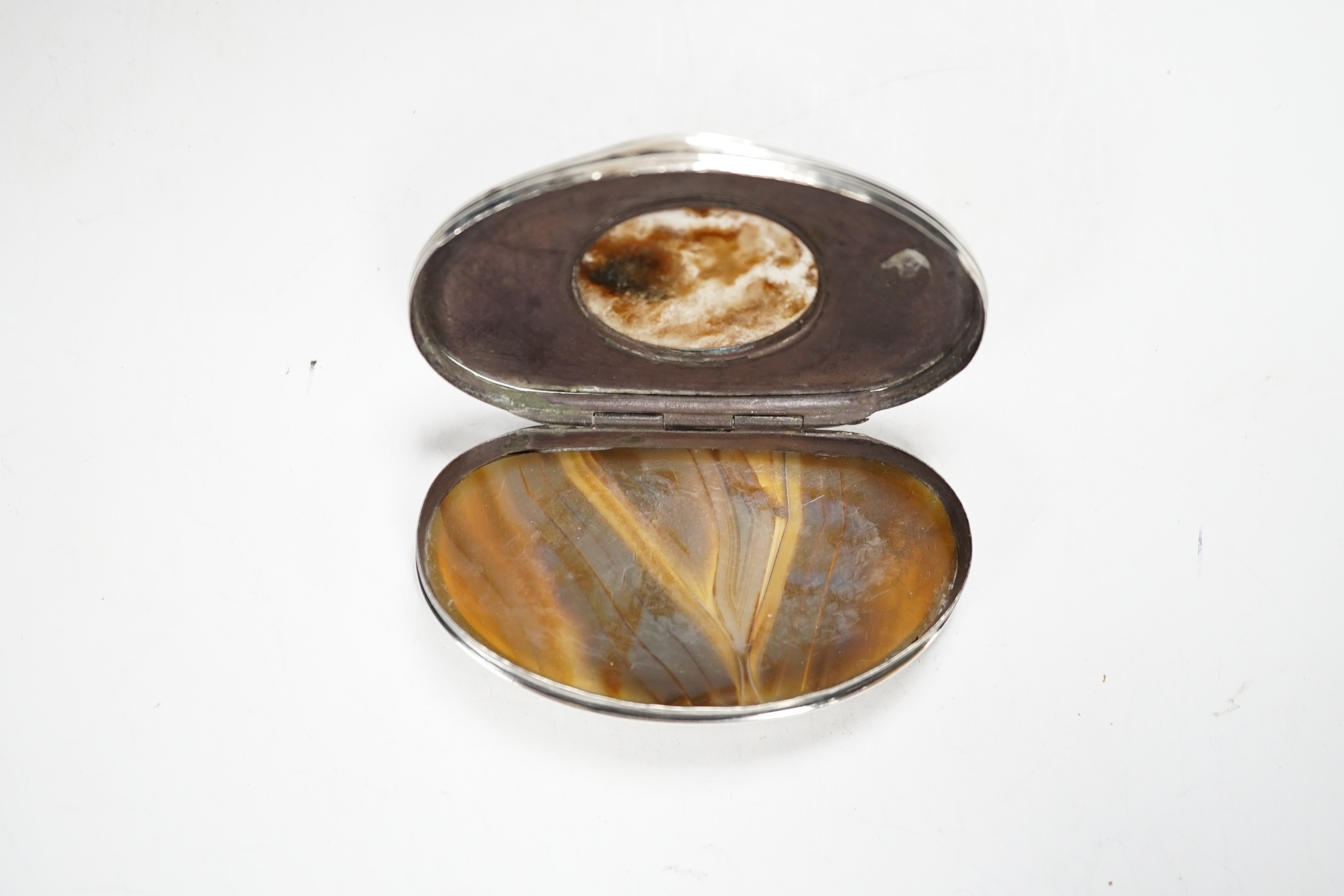 An early 19th century Scottish? white metal oval snuff box, with banded agate base and inset agate lid, decorated with dogs and scrolls, 69mm.